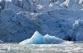 A small blue iceberg floats near the edge of the glacier.